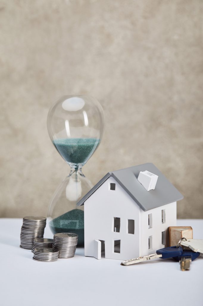 house model on white table with hourglass, silver coins and keys, real estate concept